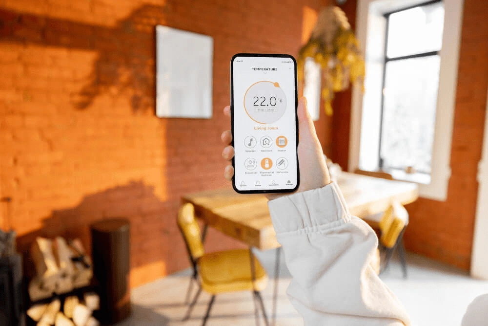 Hand hält Smartphone mit geöffneter Smart-Home-App zur Temperaturregelung im gemütlichen Wohnzimmer.