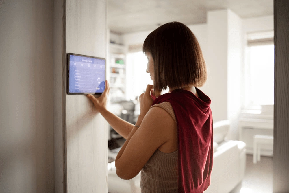 Frau nutzt ein Wand-Touchpanel zur Steuerung von Temperatur und Licht im vernetzten Wohnzimmer.
