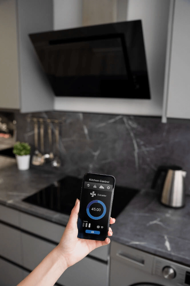 Hand hält ein Smartphone mit geöffneter Smart-Home-App zur Steuerung der Dunstabzugshaube in einer modernen Küche.